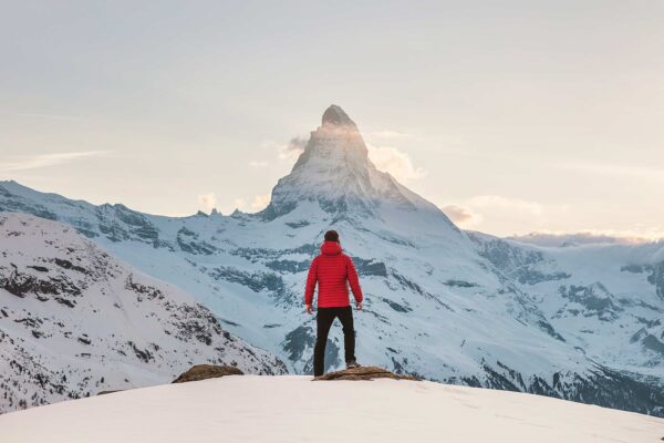 Mann in roter Jacke tagsüber auf verschneiten Berg